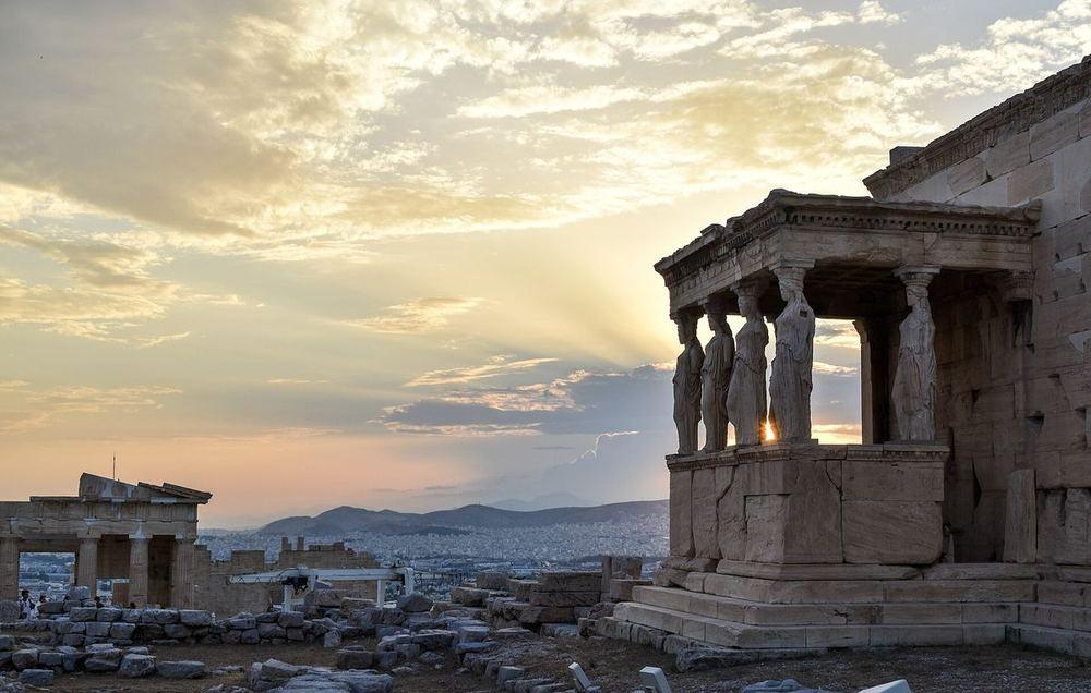 The Caryatid porch of the Erechtheion on the Acropolis: six marble women standing in place of columns, backlit by the setting sun
