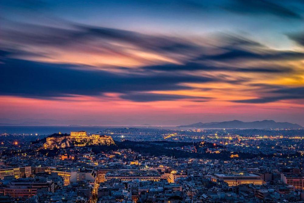 Athens at dusk from the top of Lycabettus hill: the lit Acropolis on its rock, the city spread out to the sea, a violet and orange sky