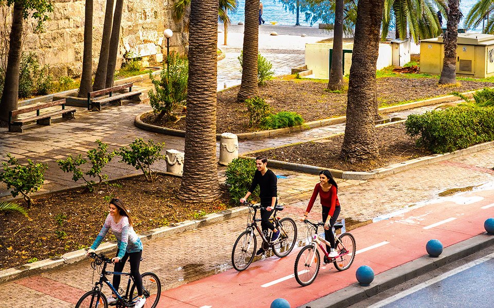 Cyclists on a marked bike path beside the walls of Neratzia castle in Kos town, palm trees along the route