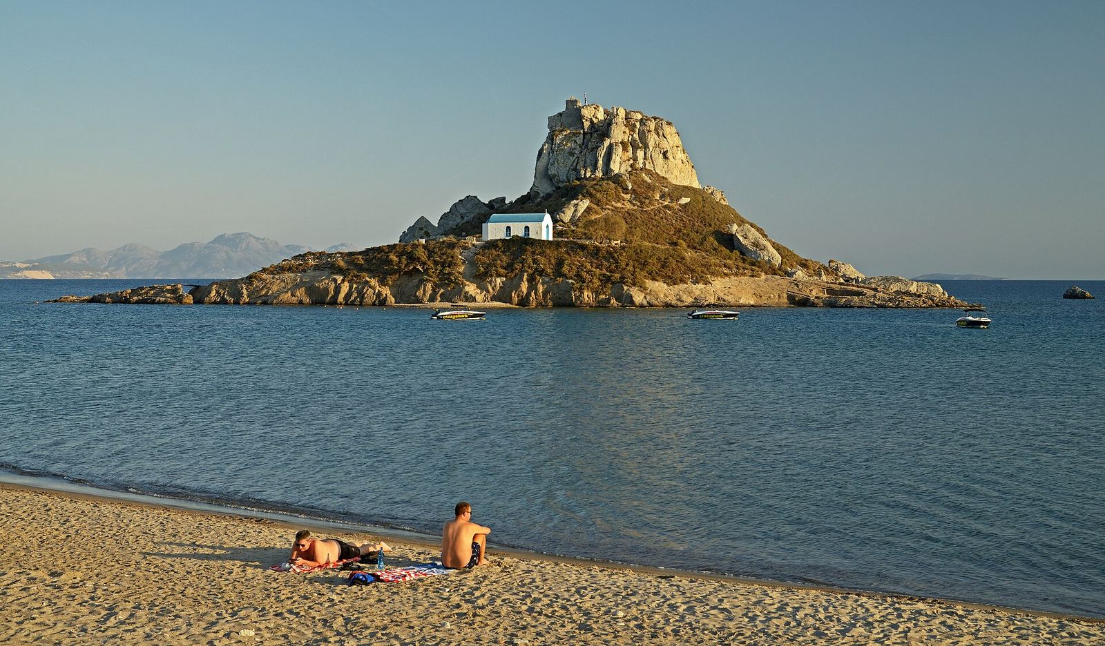The islet of Kastri with its white chapel offshore, seen from the sand at Kefalos bay in evening light