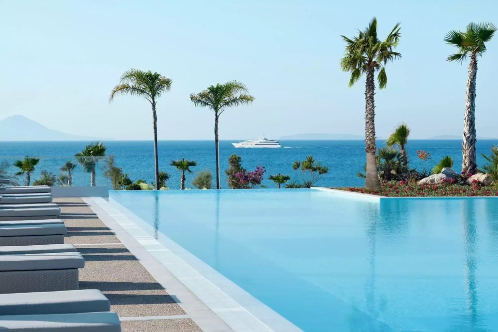 The pool terrace at a large family resort on Kos: sunbeds in a row, palm trees, the sea beyond