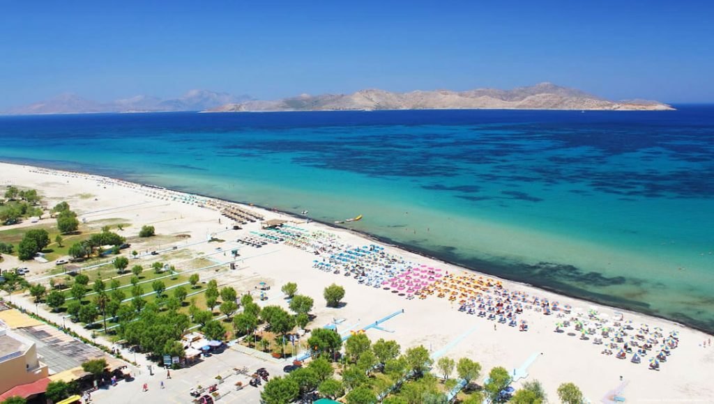 Tingaki beach on Kos: a long flat strip of pale sand with rows of umbrellas and very shallow turquoise water