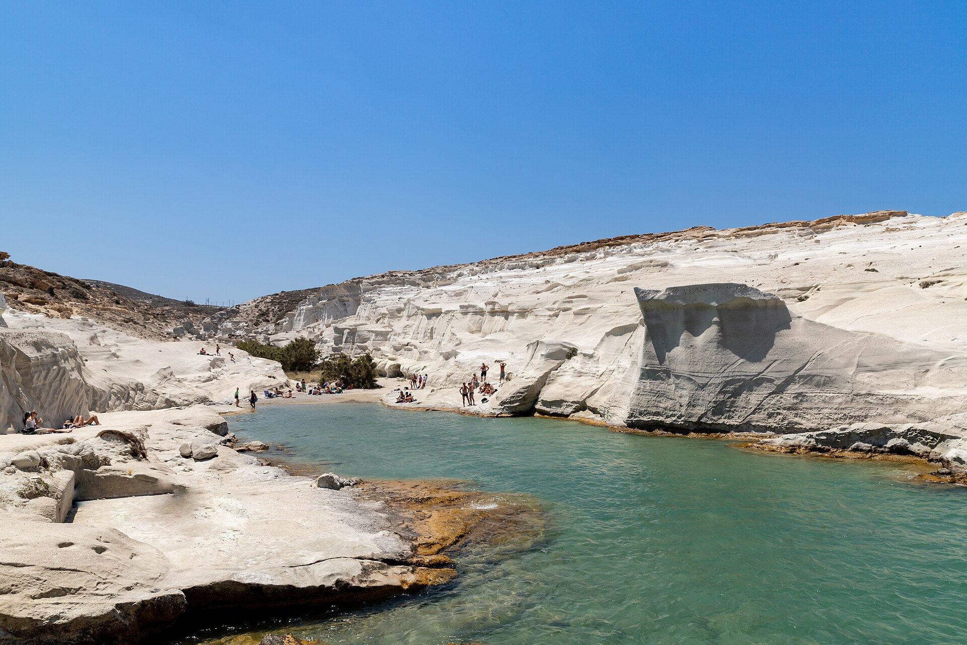 Sarakiniko on Milos: white volcanic rock worn smooth into ridges and hollows, with a turquoise inlet cutting through the middle
