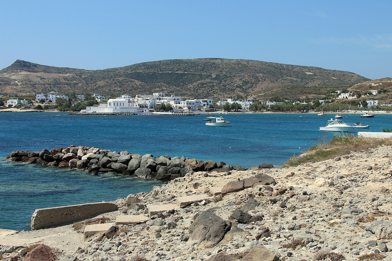 Pollonia on Milos seen across the bay, a low white village along the shore with fishing boats moored in front