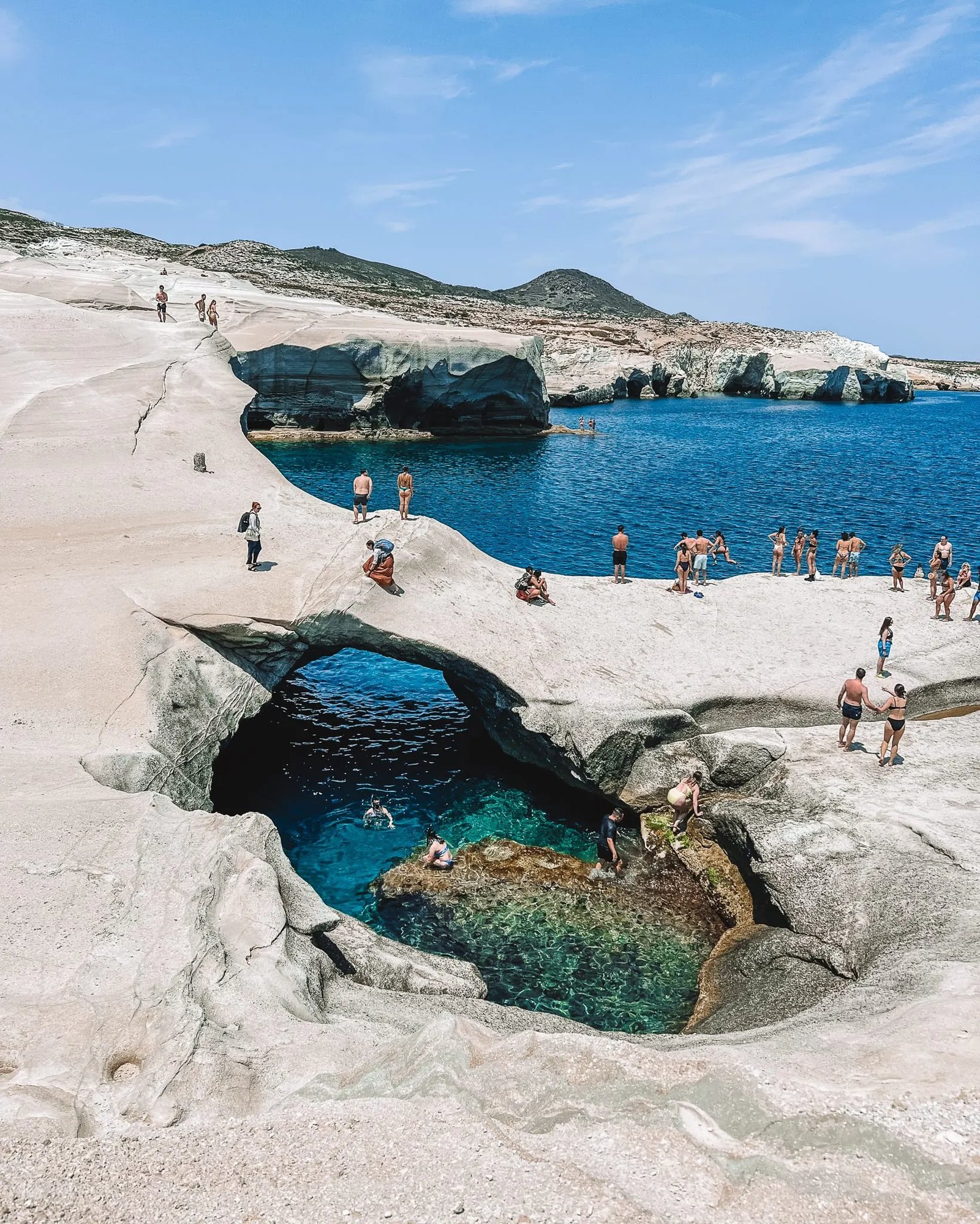 Sarakiniko on Milos: people swimming in a narrow inlet cut through smooth white volcanic rock