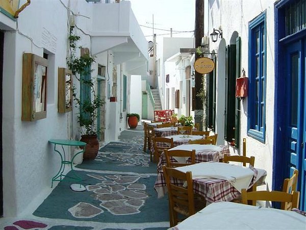 A taverna lane on Milos with tables set under an awning and whitewashed walls either side