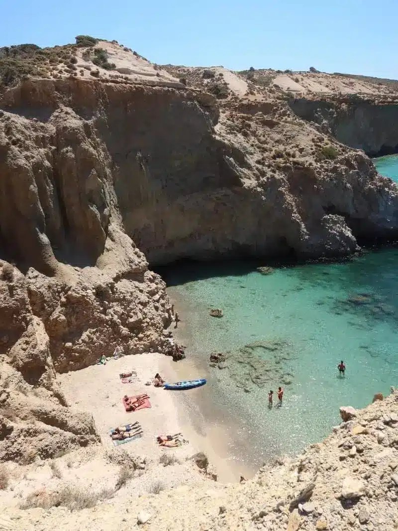 Tsigrado beach on Milos: a small sand cove enclosed by cliffs, reached by a rope and a wooden ladder through a crevice