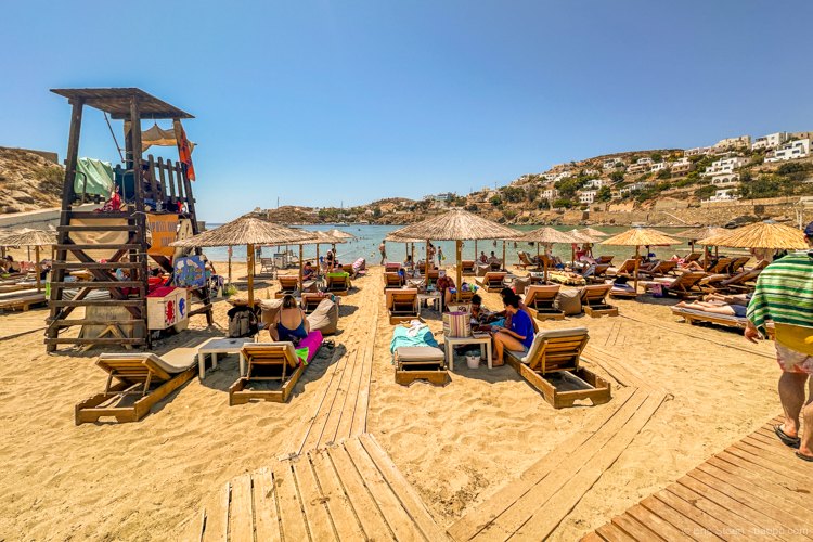 An organized beach on Syros with wooden sunbeds, straw umbrellas, a lifeguard tower and shallow water