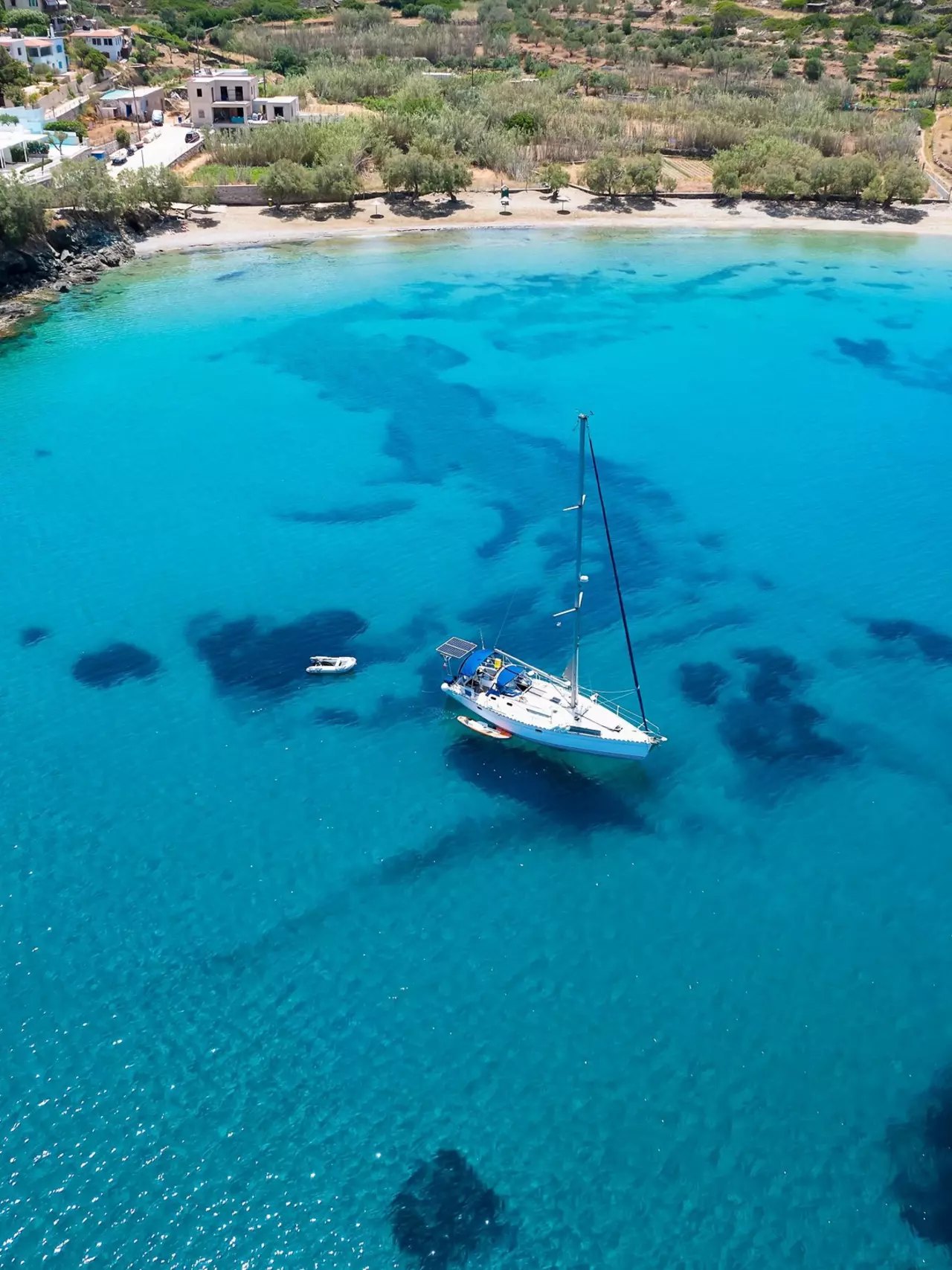 A turquoise cove on Syros seen from above with a single sailboat anchored in clear water
